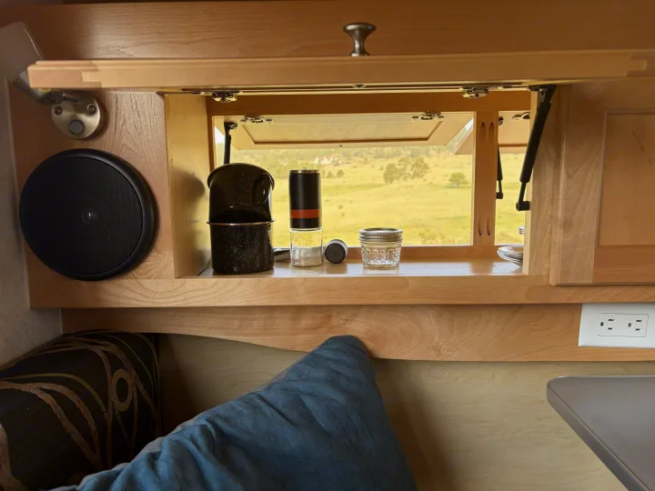 Cozy RV rental interior with an open window framing a sunny field view. Coffee setup, speaker, and outlets make it homey.. nuCamp T@B CS-S 2017