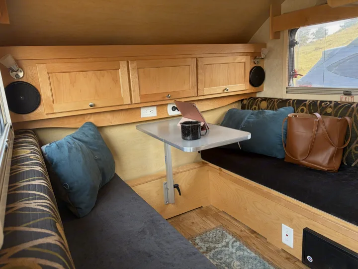 Inside a cozy rv rental, featuring light wood cabinetry, a dinette table, and plush bench seating with pillows.. nuCamp T@B CS-S 2017