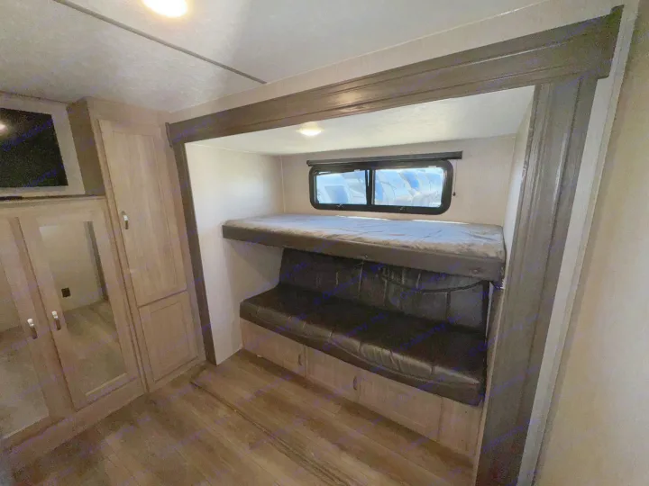 This RV rental interior features a bunk bed over a couch, with a wardrobe and TV visible left. A cozy space for travelers.. Coachmen Freedom Express 320BHDSLE 2021