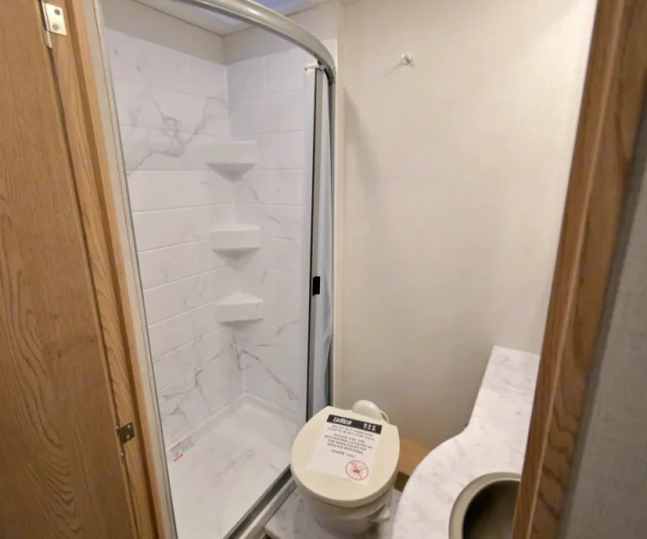 RV rental bathroom: compact shower with marble-look walls & shelves, a toilet, and a vanity area.. Thor Chateau 2026