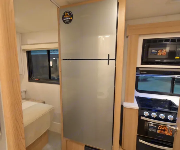 Inside an rv rental: modern kitchen with stainless fridge, microwave, oven, and window view to a sleeping area.. Thor Chateau 2026
