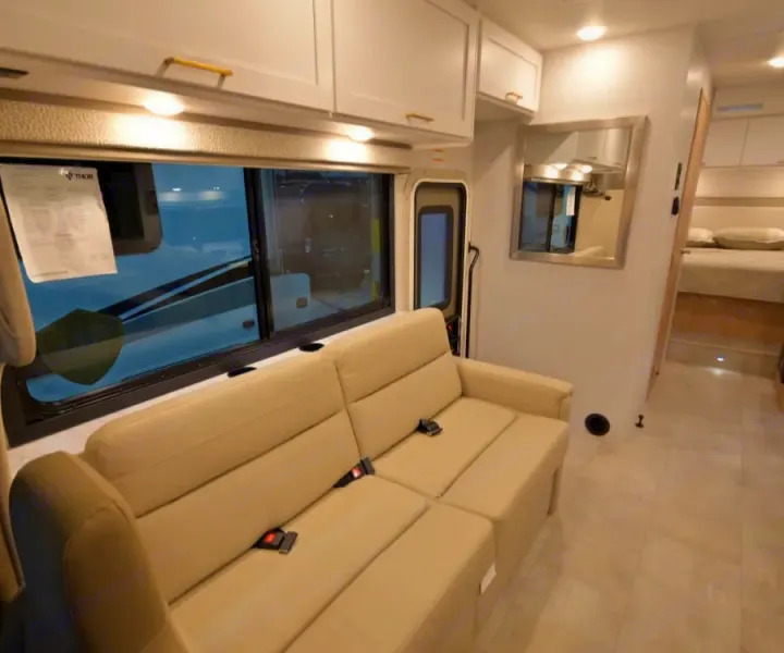 Explore this bright RV rental interior featuring a comfy sofa, large window, overhead storage, and a private bedroom beyond.. Thor Chateau 2026