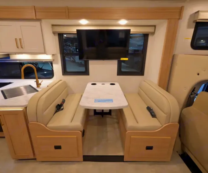 Well-appointed RV rental interior: Light wood & cream dinette with kitchen and TV. Compact motorhome space for travel.. Thor Chateau 2026