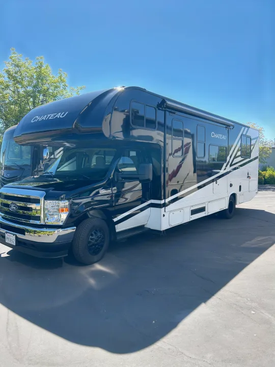 This modern black and white Chateau Class C rv rental, with diagonal stripes, is parked on asphalt under a clear sky.. Thor Chateau 2026