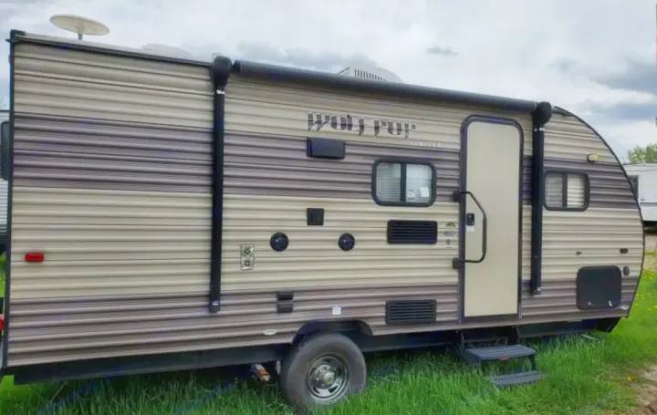 Side view of a striped Wolf Pup travel trailer RV rental. Features include an awning, windows, door, and a roof-mounted dish.. Forest River Cherokee Wolf Pup 2018