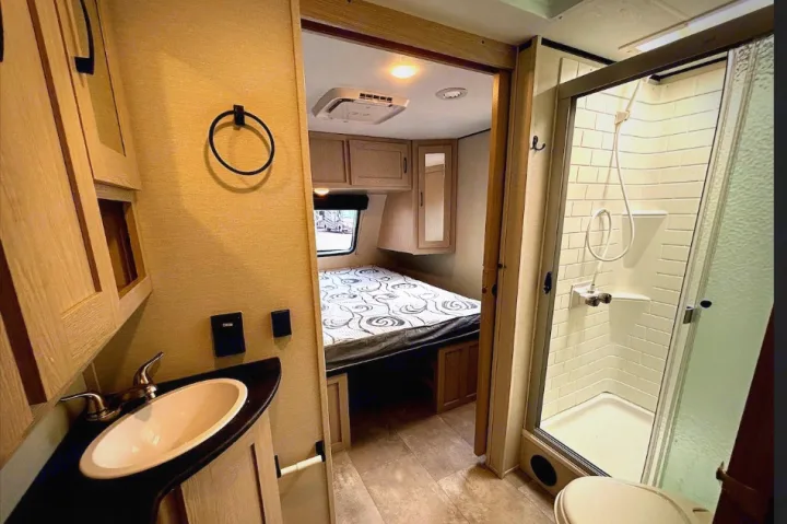 RV rental interior featuring a compact bathroom with sink, shower, & toilet, and a cozy bedroom.. Coachmen Apex 2022