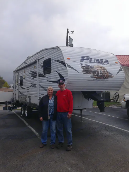 A happy couple poses by their large Puma travel trailer rv rental, perfect for upcoming travel and adventures.. Palomino Puma 2010