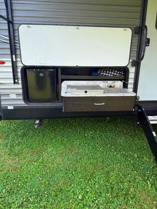 An RV rental's open outdoor kitchen features a mini-fridge, pull-out sink, and two-burner stove for convenient camping.. Jayco Jay Flight 2021