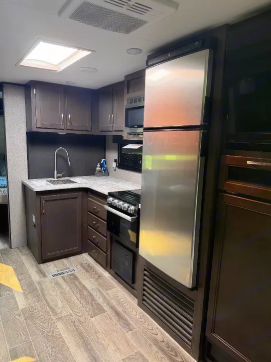 RV rental kitchen: stainless steel appliances (fridge, microwave, stove), sink, dark cabinets, skylight, and wood-look floor.. Jayco Jay Flight 2021