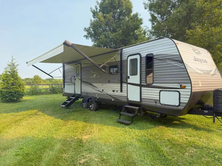 An RV rental: a grey and white Jayco travel trailer, sits on green grass with its awning extended and steps down.. Jayco Jay Flight 2021
