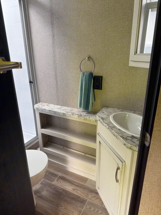 This clean RV rental bathroom features a sink with a vanity, toilet, shower, and convenient open shelving for storage.. Jayco Jay Flight 2021