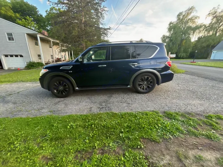 A dark blue SUV is parked on a driveway. Great for family travel, a versatile option compared to an RV rental.. Nissan 2017 Nissan Armada Platinum 4WD V8 2017