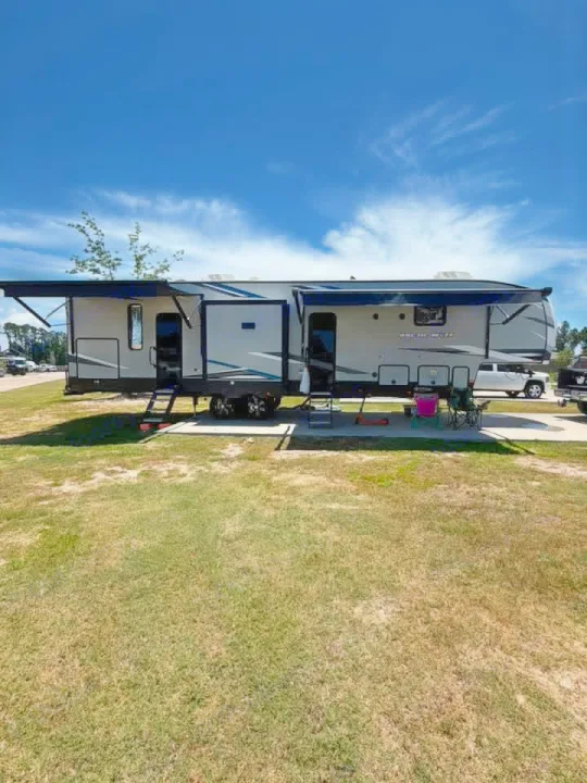 RV rental: a spacious fifth-wheel trailer with extended slide-outs and awnings, parked on a sunny grassy site.. Forest River Artic wolf 2022