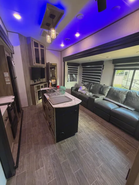 Explore this RV rental's inviting interior: sleek kitchen island, cozy gray sectional, and ambient blue lighting for a great trip.. Forest River Artic wolf 2022