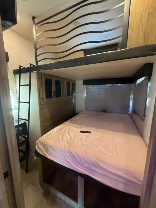 Compact RV rental bedroom with a comfy bed, overhead cabinets, and a loft bunk bed with ladder, optimized for space.. Forest River Artic wolf 2022