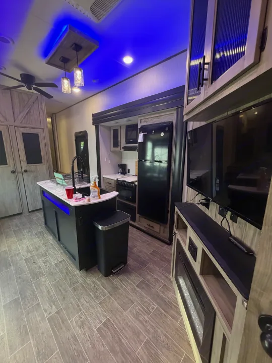 Modern RV rental interior: kitchen with island sink, full appliances, sleek entertainment center, and cool blue ambient lighting.. Forest River Artic wolf 2022