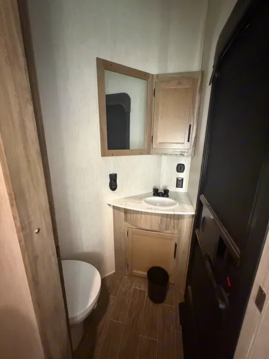 Compact RV rental bathroom features corner vanity, sink, toilet, and mirror for efficiency.. Forest River Artic wolf 2022