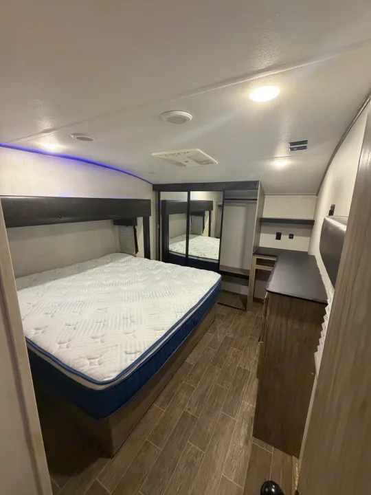 Spacious RV rental bedroom featuring a queen bed, wood floors, mirrored closet, ceiling AC, and accent lighting.. Forest River Artic wolf 2022