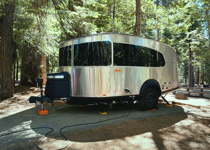 Modern Airstream-style rv rental trailer nestled in a sun-dappled forest campsite, fully set up with power. Ready for adventure.. Airstream Basemamp 2025