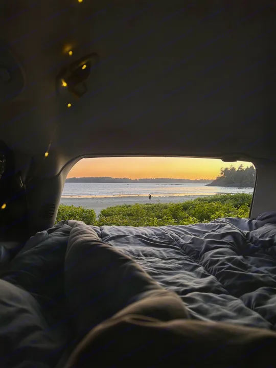 A serene sunset view over a beach from a cozy RV rental bed, complete with fairy lights. Ideal for van life adventure.. Dodge Grand Caravan 2005