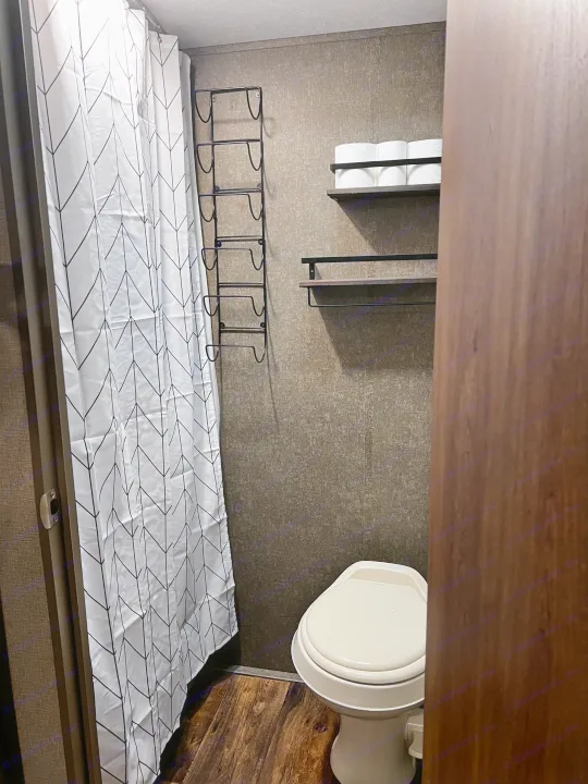 This RV rental bathroom features a white geometric shower curtain, toilet, wall-mounted organizer, and TP shelves.. Keystone RV Summerland Mini 2017