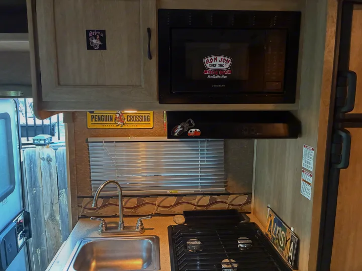 RV rental kitchen interior, showing a microwave, sink, stove, and personalized decorations like a "Ron Jon Surf Shop" sticker.. Forest River Coachmen Freelander 2015