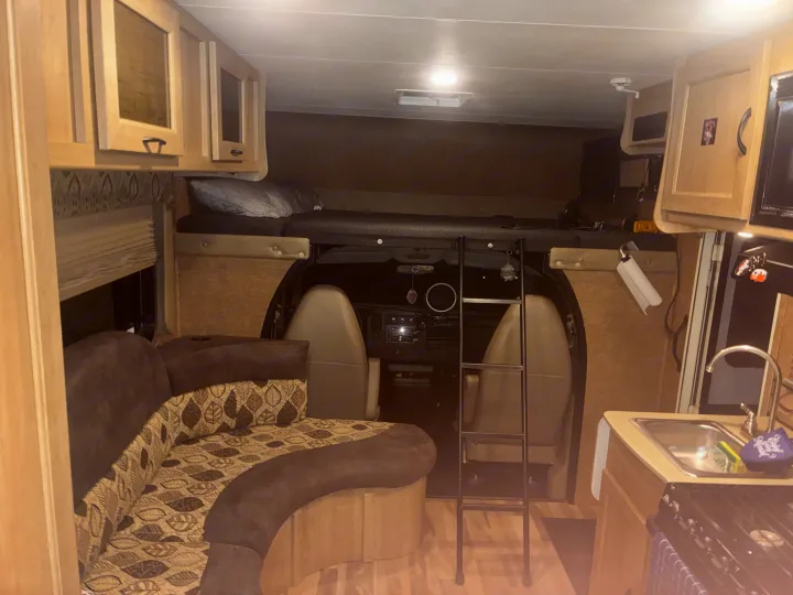 RV rental interior: overhead bunk with ladder, kitchen area with sink & stove, plus a cozy dinette with patterned cushions.. Forest River Coachmen Freelander 2015