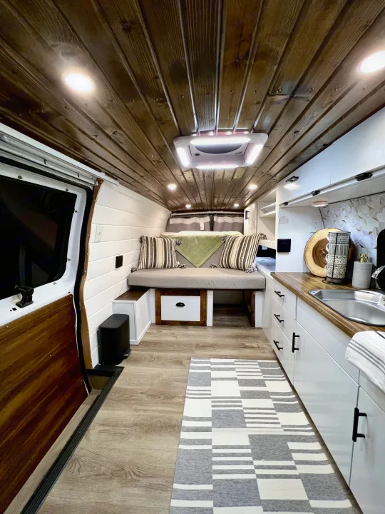 Interior of an inviting rv rental van with a warm wood plank ceiling, modern kitchenette, and cozy bench seating.. Ford Ford E350 2005