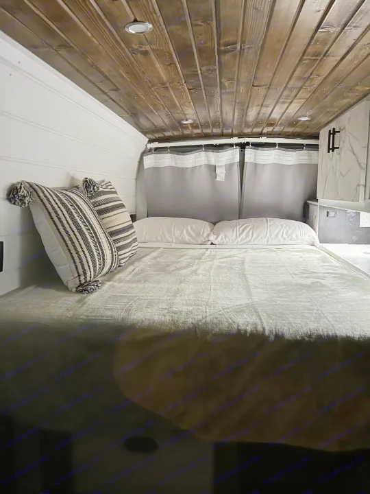 Cozy RV rental bedroom with a wooden ceiling, white walls, comfortable bed, and stylish striped pillows.. Ford Ford E350 2005