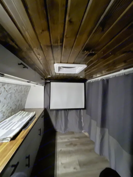 RV rental interior: wooden ceiling, pull-down projector screen, and gray curtains create a cozy media space in this camper van.. Ford Ford E350 2005