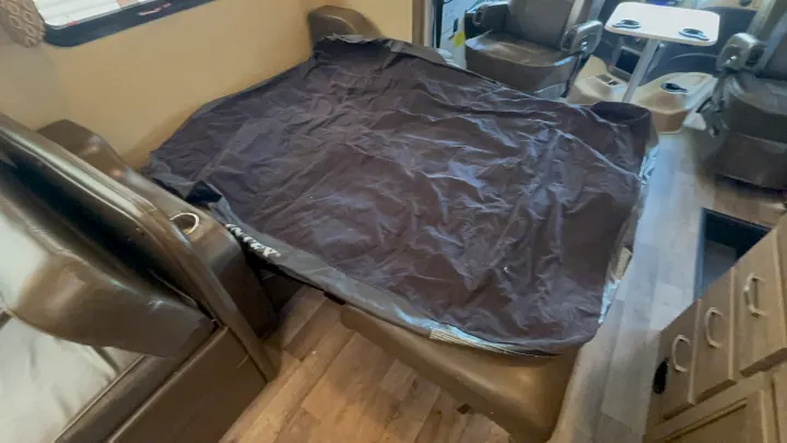 Inside an RV rental: A crumpled dark cover rests on interior seating. Captain's chairs, a table, and cabinets are visible.. Jayco Precept 2019