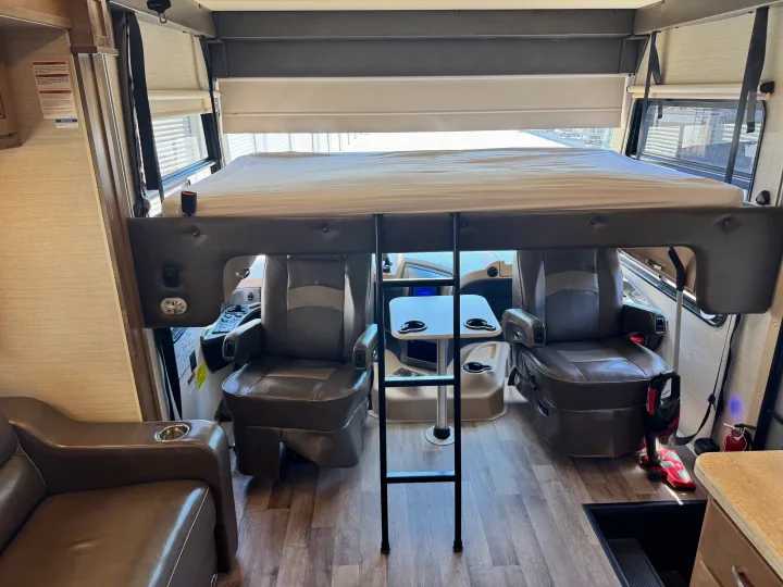Spacious RV rental interior featuring an overhead bunk bed with a ladder, captain's chairs, and a small table.. Jayco Precept 2019