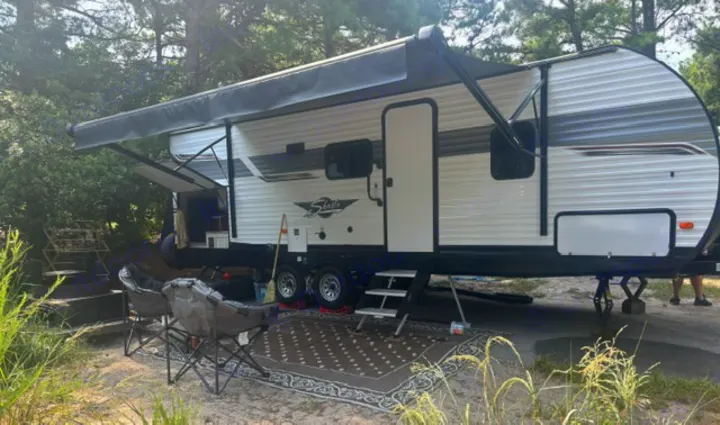 This rv rental travel trailer is set up at a campsite with an extended awning, outdoor rug, and chairs.. Forest River Shasta 2022