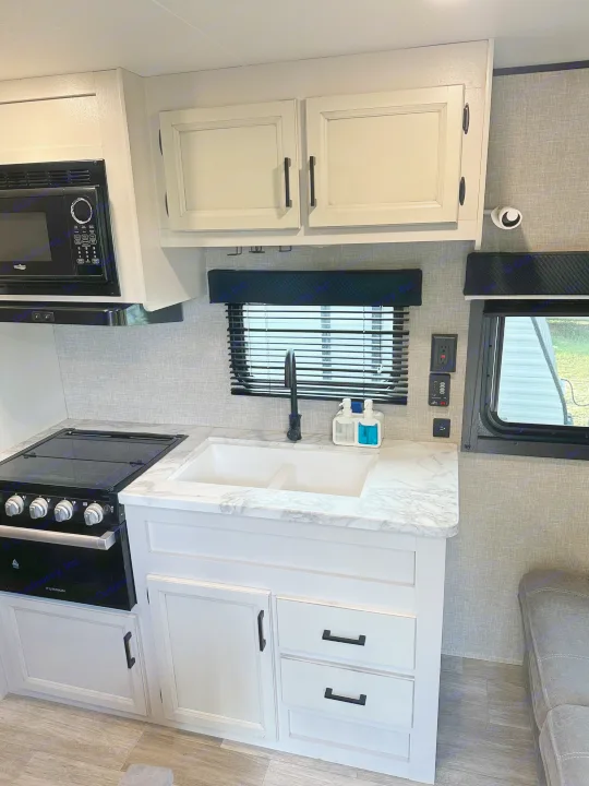 Modern rv rental kitchen with white cabinets, marble countertop, black sink, stove, and microwave. Clean and functional space.. Jayco Jay Flight 2023