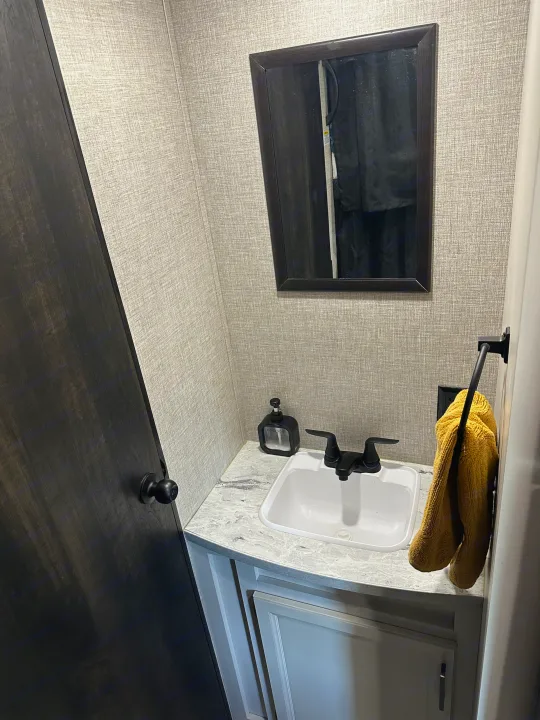 RV rental bathroom with textured walls, dark door, vanity, sink, mirror, black fixtures, and a yellow towel.. Jayco Jay Flight 2023