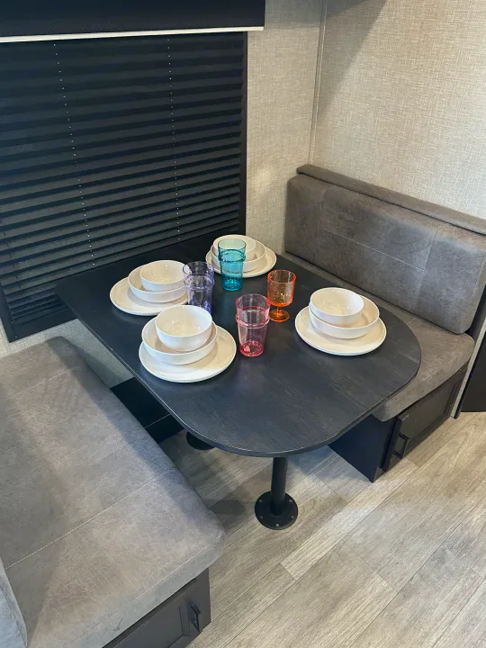 RV rental dinette with a dark table, gray bench seating, white dishes, and colorful glasses.. Jayco Jay Flight 2023