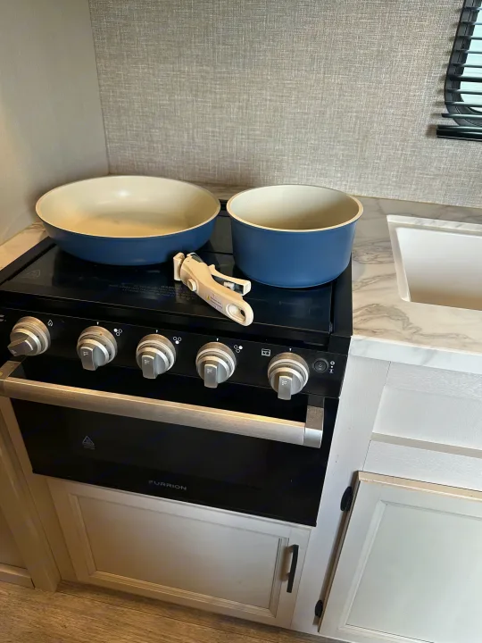 Functional RV rental kitchen with Furrion stove/oven, sink, and blue ceramic pots/pans on cooktop, plus a removable handle.. Jayco Jay Flight 2023