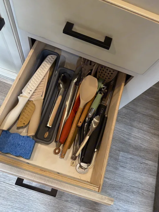 Open kitchen drawer in an RV rental, showing various utensils like spatulas, tongs, and knives, plus a blue sponge.. Jayco Jay Flight 2023