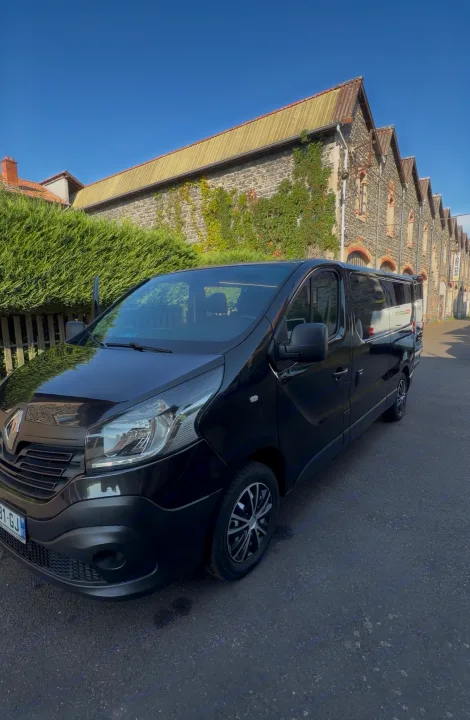 A black passenger van, parked on a sunny street next to an ivy-covered stone building. Perfect for your spacious rv rental needs!. Renault TRAFIC 2019