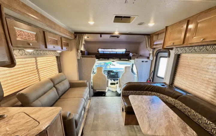 Spacious RV rental interior with a cozy living area, dinette, and ample overhead storage, leading to the cab.. Forest River Coachmen Leprechaun 2020