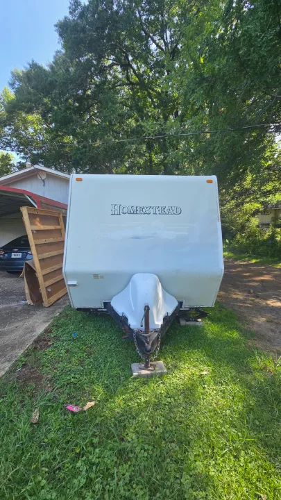 White Homestead travel trailer, ideal for rv rental, parked on grass. A car is visible under a nearby carport.. Starcraft Homestead Settler 2004