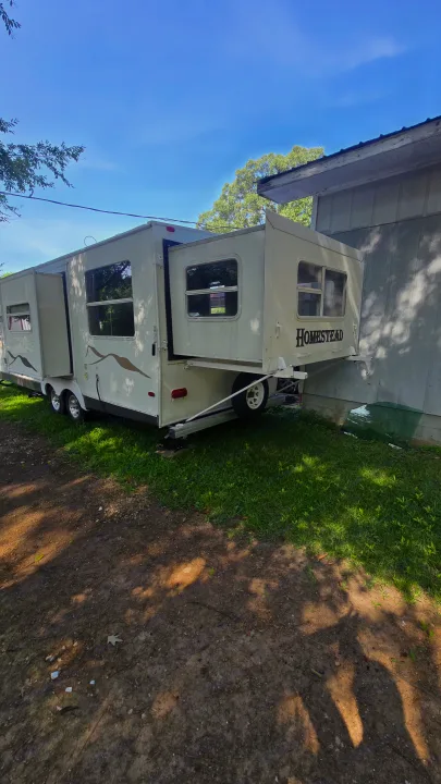 Homestead RV rental: A travel trailer with extended slide-outs, parked on grass beside a building under a blue sky.. Starcraft Homestead Settler 2004