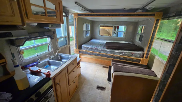 RV rental interior showing a kitchen with sink, stove, and cabinets, adjacent to a cozy sleeping alcove with a bed.. Starcraft Homestead Settler 2004