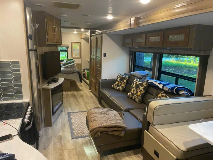 Spacious and modern RV rental interior featuring a cozy living area with sofa, kitchen, and bedroom in the background.. Coachmen Mirada 32ss 2020