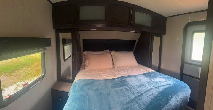Cozy RV rental bedroom with a comfy bed, dark overhead cabinets, and windows, ideal for travel.. Kodiak Ultimate 288BHSL 2018