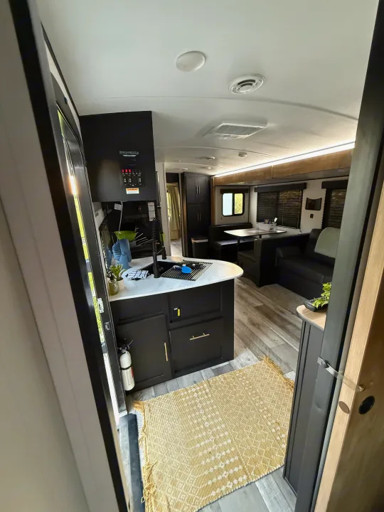 Modern RV rental interior with black kitchen cabinets, dining booth, and sofa, showcasing spacious living.. Keystone RV Springdale 2022
