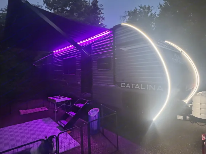 Evening at an RV rental: a modern travel trailer with vibrant purple and white LED lighting under a dark sky, steps, and a pet area.. Coachmen Catalina Summit Series 8 2026