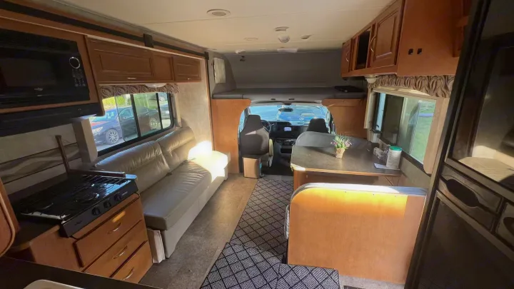 Cozy RV rental interior: microwave, stovetop, sofa, dining table, driver's cab, and an overhead bunk for travelers.. Itasca Spirit 2014