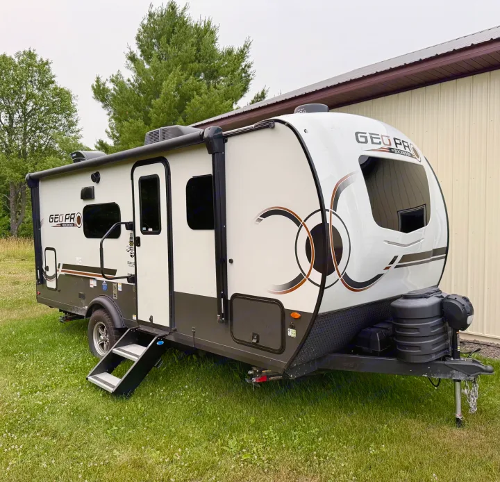 A modern white & dark grey Geo Pro travel trailer RV rental, parked on green grass next to a building, ready for adventure.. Forest River Rockwood Geo Pro 2025
