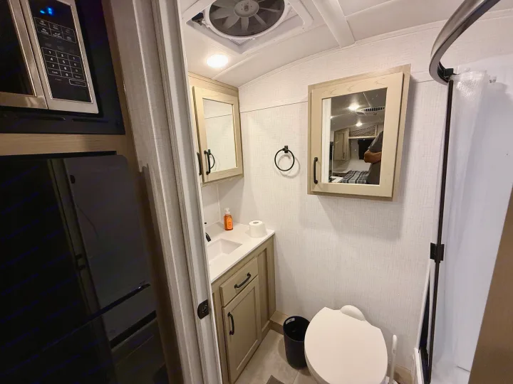 Compact rv rental bathroom: sink, vanity, toilet, shower. Microwave visible; living area reflected in mirror.. Forest River Rockwood Geo Pro 2025